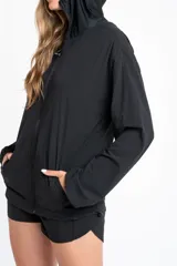 Campera deportiva de color negro con cierre frontal, capucha y mangas largas con puños elásticos. Presenta una textura ligera y un corte ajustado al cuerpo.