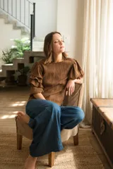 Blusa de tela texturizada color café, con cuello redondo y mangas al codo que presentan tres volados superpuestos y puños elásticos. Cuenta con cierre de botón en la parte posterior.