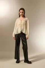 Blusa de poliéster color natural, con cuello en V, mangas largas con puños elásticos y detalle de frunces con cordón ajustable en el frente.