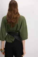 Camisa de corte holgado en color beige, con cuello solapa, escote en pico y mangas cortas amplias. Presenta cierre frontal con botones a tono.