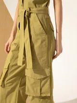 Mono color verde oliva, con cuello camisero, sin mangas, bolsillos frontales y laterales tipo cargo, y cinturón de lazo.