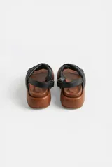 Sandalias de plataforma con capellada de tiras cruzadas acolchadas de cuero color negro, base marrón de goma EVA y tira trasera con ajuste mediante hebilla metálica.