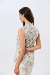 Camisa sin mangas de lino y algodón, con estampado floral en tonos violeta y verde sobre base beige, cuello camisero y cierre frontal de botones.