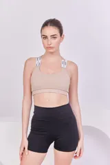 Top deportivo color beige con espalda cruzada, elástico en la base y tiras regulables con logo de la marca.