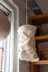 Luminaria cilíndrica tubular de fieltro artesanal 100% lana merino color natural, con un aro de hierro de 28cm de diámetro y un paño de fieltro Nuno de 55cm de alto con efecto arrugado y borde de terminación orgánica.