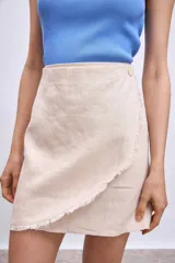 Minifalda color beige de corte evasé con diseño cruzado y detalle de flecos en el ruedo.