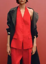 Chaleco rojo de lino con cuello halter, sin mangas, corte entallado, cierre frontal con botones y dos bolsillos de solapa laterales.