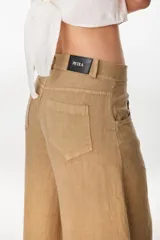 Pantalón de lino color tostado, de corte ancho y silueta holgada, con bolsillos traseros aplicados y etiqueta de marca en la cintura.