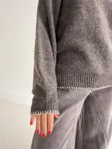 Sweater de punto color gris con cuello redondo, mangas largas y terminaciones con detalle de pespunte en color crudo en el cuello, puños y ruedo.