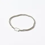 Pulsera elástica de cuentas plateadas con dije rectangular plateado.