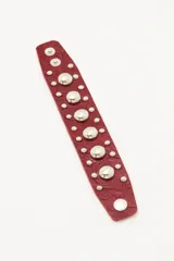 Pulsera de cuero vacuno color bordó con textura grabada, decorada con tachas metálicas plateadas de distintos tamaños y cierre con broches a presión.