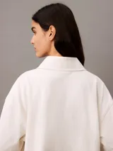 Chomba color crema de punto de algodón con cuello clásico, tapeta de botones oculta y mangas cortas. Presenta un corte holgado y un escudo bordado con el logo de Calvin Klein en el pecho.