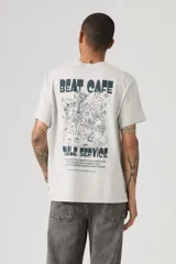 Remera gris melange de corte relaxed fit, con cuello redondo, mangas cortas y estampa pequeña en el pecho con motivo de taza de café y la inscripción "Beat Cafe".