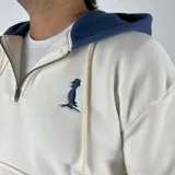 Canguro blanco hueso de algodón con felpa, capucha forrada en azul marino, cierre parcial con cremallera, cordón ajustable y bolsillo tipo canguro con solapa.