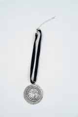 Gargantilla de cinta de terciopelo negro con dije circular de metal plateado con textura rugosa.