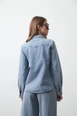 Camisa de jean color azul claro con tachas metálicas en el canesú y a lo largo de las costuras frontales. Tiene mangas largas con puños abullonados y cierre frontal con botones.