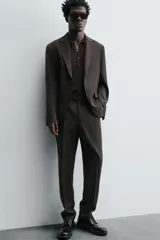 Pantalón de traje regular fit confeccionado en tejido de lana. Presenta bolsillos frontales, bolsillos traseros de vivo con botón y cierre frontal con cremallera y botón.