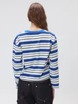 Remera de manga larga con diseño a rayas horizontales en tonos azul, blanco y negro. Presenta un cuello redondo al tono y un logo bordado en el pecho. El diseño destaca por tener un patrón de rayas diferente en las mangas y un calce holgado.