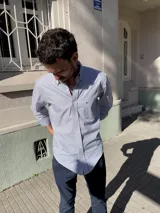 Camisa de corte clásico con diseño a rayas verticales celestes y blancas, de manga larga, cuello abotonado y bolsillo frontal en el pecho.
