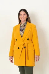 Chaqueta cruzada color mostaza con lazo y botones negros. Tiene bolsillos con tapa y detalle de cuatro botones en las mangas.