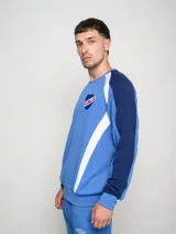 Buzo deportivo de manga larga, color principal rojo, con mangas azul marino y detalles en blanco que bajan desde el hombro hasta el puño. Presenta cuello redondo, logo Umbro y escudo del Club Nacional de Football en el pecho.