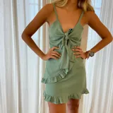Vestido corto verde con breteles finos, escote en V y detalle de nudo en el busto. Falda cruzada con volados.