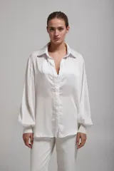 Camisa blanca de mangas largas abullonadas con puños elásticos, cuello clásico y cierre frontal con botones.