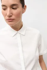 Camisa clásica blanca de manga corta, con cuello camisero y cierre frontal oculto con botones.