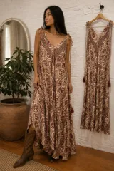 Vestido largo holgado con estampa estilo paisley y mandalas en tonos bordó y tostado sobre base beige, escote en V y tirantes finos ajustables con lazos y borlas en los extremos.