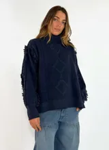 Sweater de punto color azul marino, con cuello alto, diseño de rombos en relieve y detalle de flecos en las mangas.