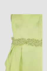 Vestido largo verde con escote asimétrico, corte ajustado y abertura lateral en la falda. Presenta detalle de volado en la cintura y adorno de pedrería.