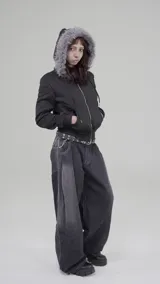Campera corta negra con capucha y cierre frontal, confeccionada en poliéster. Tiene corte boxy y piel sintética gris alrededor de la capucha.