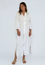 Vestido largo color beige de lino, con cuello mao, mangas 3/4 abullonadas, cierre frontal con botones y volantes verticales.