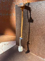 Collar con tiento de cuero marrón y dije con forma irregular, compuesto por un cilindro de metal dorado, una piedra amatista y una piedra de cuarzo transparente.