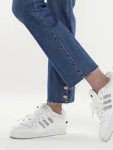 Pantalón jean azul de corte recto, con terminación desflecada y botones dorados en el ruedo.