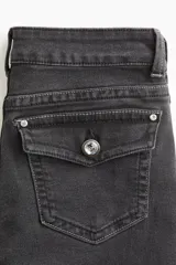 Jeans de denim negro lavado con leve stretch, tiro bajo, corte ajustado en cadera y pierna acampanada desde la rodilla. Presenta cierre y botón frontal, bolsillos abiertos delanteros y bolsillos traseros con solapa y botón.