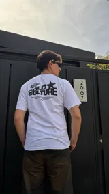 Remera blanca de algodón con estampado negro en la espalda que incluye el logo de la marca, una estrella y texto.