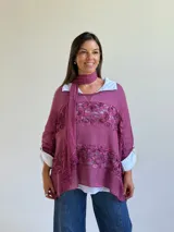 Sweater de punto magenta con diseño holgado, cuello redondo y detalles de encaje floral aplicado en el frente. Incluye una bufanda tipo choker integrada del mismo tejido.