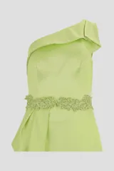 Vestido largo verde con escote asimétrico, corte ajustado y abertura lateral en la falda. Presenta detalle de volado en la cintura y adorno de pedrería.