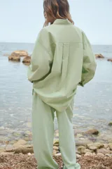 Camisa oversize de cuello solapa, manga larga con puño caído y bolsillo de plastrón en el pecho. Presenta un patrón de rayas verticales sutiles en tono verde lima.