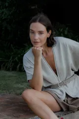 Saco de punto color beige con diseño de trenzas en los bordes frontales, manga corta y corte holgado. Presenta un estilo versátil ideal para diversas ocasiones.