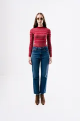 Top de punto ajustado al cuerpo, con cuello redondo y manga larga. Presenta un diseño de estampado geométrico a cuadros en tonos rojos y rosados.