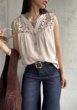 Blusa beige sin mangas con detalle de encaje en el cuello y botones en el frente.