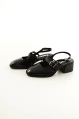 Zapatos tipo Mary Jane de charol color negro, con taco bloque, talón descubierto y doble tira frontal con hebillas metálicas.