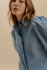 Camisa de denim con mangas abullonadas y cierre frontal con botones. Presenta un diseño de calce cómodo con estructura definida.