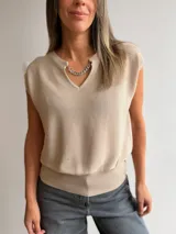 Musculosa de tejido de punto color beige con escote en V y detalle de cadena metálica desmontable en el cuello. Presenta un diseño holgado con ruedo ajustado y mangas cortas.
