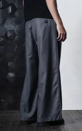 Pantalón sastrero de corte oversize en color gris, confeccionado en tejido premium con caída estructurada. Presenta dos pinzas frontales profundas, cintura ancha, bolsillos laterales y bolsillos traseros tipo ojal. Incluye detalles de botones en el ruedo.