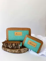 Billetera compacta de cuero con diseño bicolor en turquesa y marrón, con textura tipo reptil. Cuenta con cierre metálico perimetral y parche frontal con el logo de la marca.