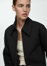 Chaqueta negra de diseño oversize con cuello camisero y cierre frontal de cremallera. Cuenta con forro interior y bolsillos laterales.