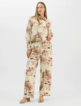 Conjunto de dos piezas compuesto por camisa de manga larga con cuello solapa y botones frontales, y pantalón de tiro alto con pierna recta y bolsillos laterales. Ambas prendas presentan un estampado paisajístico en tonos marrones sobre fondo crema.